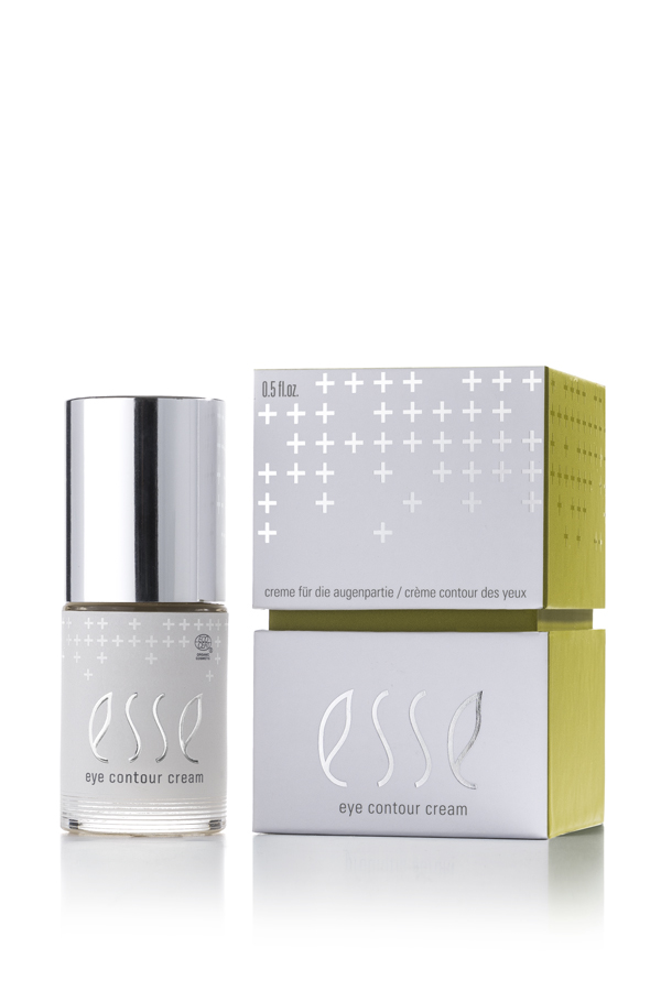 A glass bottle of Esse Eye Contour Cream with a silver cap stands beside its white and green minimalist box, both displaying the Esse name and plus sign patterns.