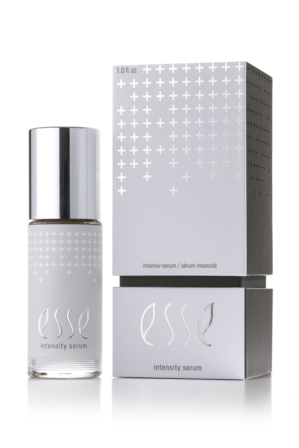 A bottle of Esse Intensity Serum with a silver cap is displayed beside its matching silver and white box, both featuring minimalist branding and subtle cross patterns.