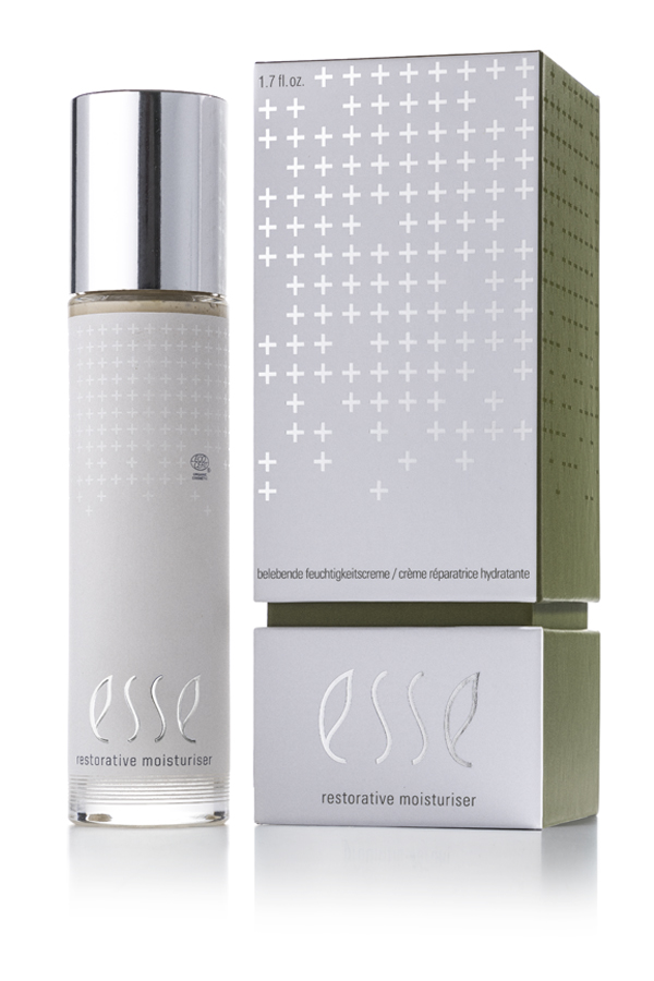 A bottle of Esse Restorative Moisturiser with a shiny silver cap stands beside its matching box, both displaying a minimalist design with silver and white cross patterns and product details.