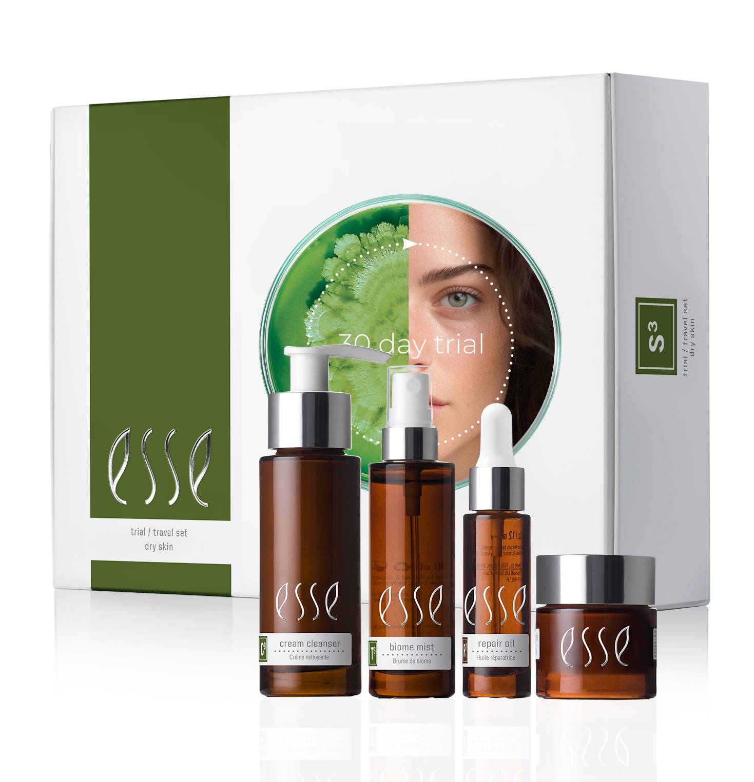 The image depicts the Esse Dry Skin Trial / Travel Set, a collection of skincare products that includes a cream cleanser, biogen mist, repair oil, and cream. The packaging sports an elegant green-and-white design with a circular cutout showcasing an image of a woman's face alongside a leaf.