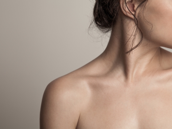 Close-up of a woman's bare shoulder, neck, and part of her face, with hair loosely tied back against a neutral background, highlighting the natural beauty and balance of her skin microbiome.